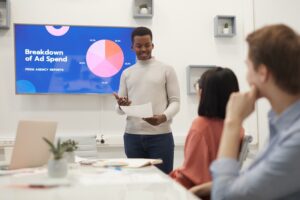 Portrait of young African man giving presentation on marketing during business meeting in modern office, copy space