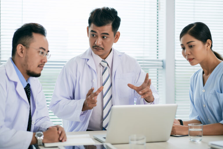 Three healthcare professionals reviewing AHPRA advertising guidelines on a laptop during a team meeting
