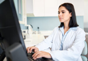 Dentist in a white coat typing on a computer in a dental clinic, reviewing AI Overviews for dentists and search visibility