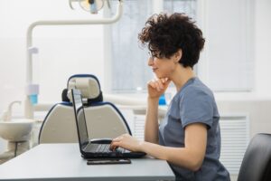 Dental professional in scrubs checking her practice’s AI search visibility on a laptop in a dental surgery