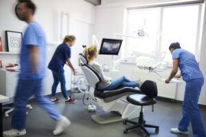 Dental team in blue scrubs preparing a patient in the chair beside a panoramic X-ray screen, illustrating a dental practice marketing audit