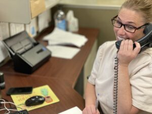 Smiling receptionist on a desk phone taking a call at a front office desk, showing how Google Business Profile posts can drive phone enquiries