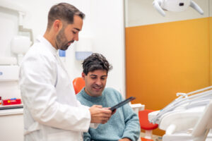 Dentist showing a returning patient his treatment plan on a tablet during a patient reactivation appointment in a dental clinic