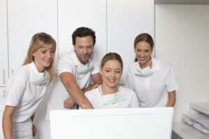 Dental team in white uniforms looking at a computer screen together while researching SEO keywords for dentists