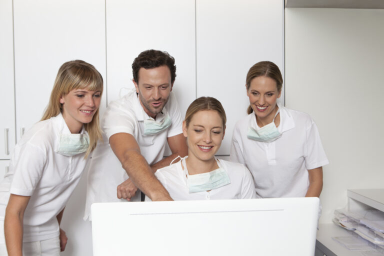 Dental team in white uniforms looking at a computer screen together while researching SEO keywords for dentists